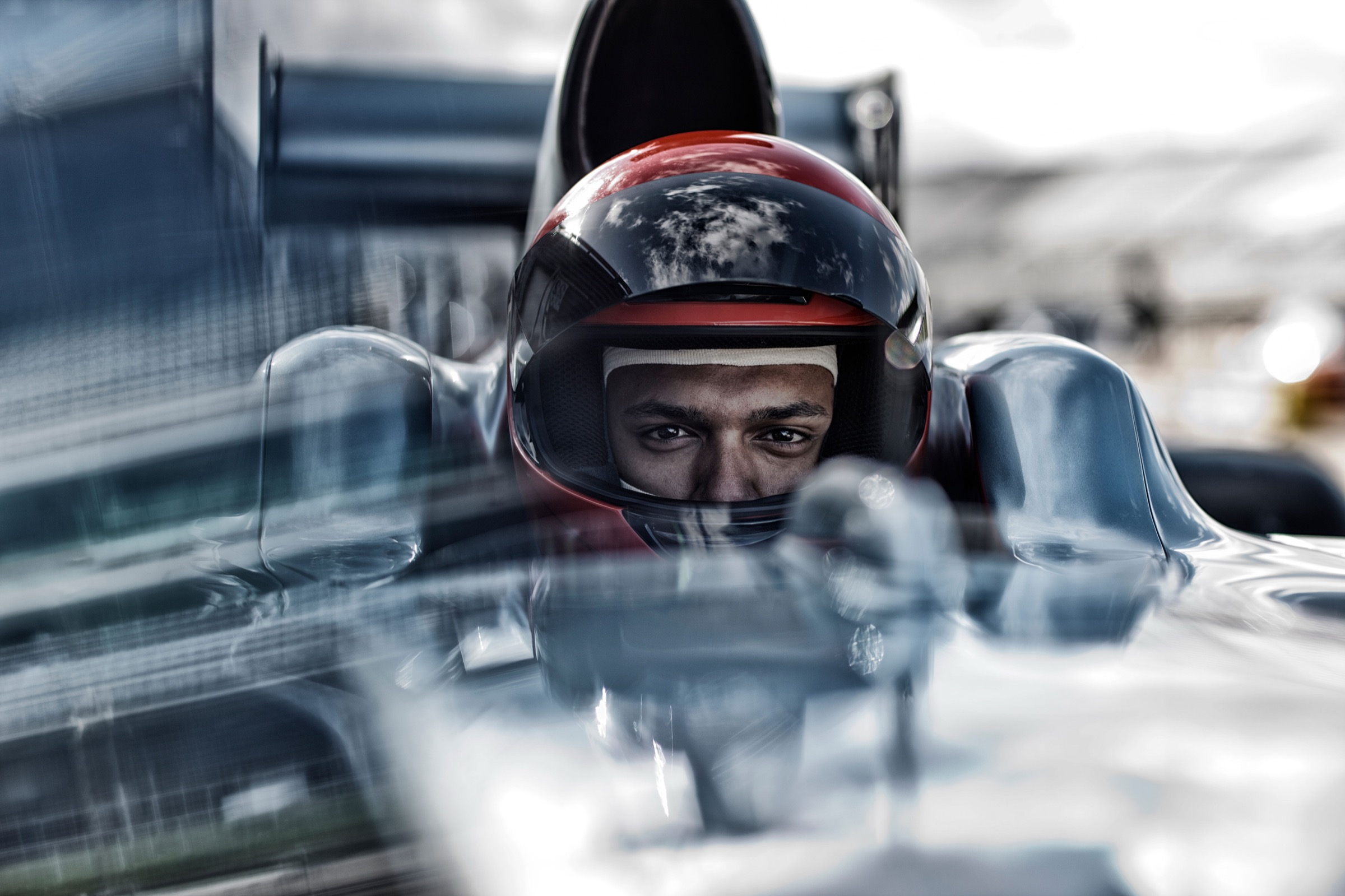 Rennfahrer im Cockpit eines Formel-Wagens, konzentrierter Blick durchs Visier